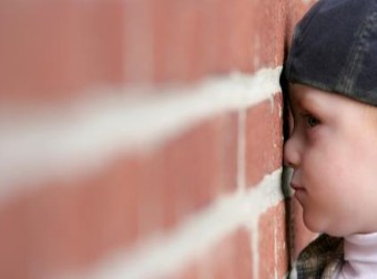 A young boy pressing his head against a brick wall